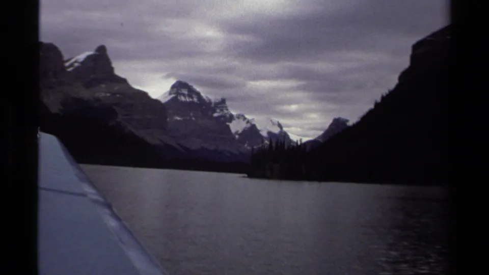 1979 British Columbia 8mm view from a boat across a calm lake toward mountains, evergreen shoreline, and an overcast sky.