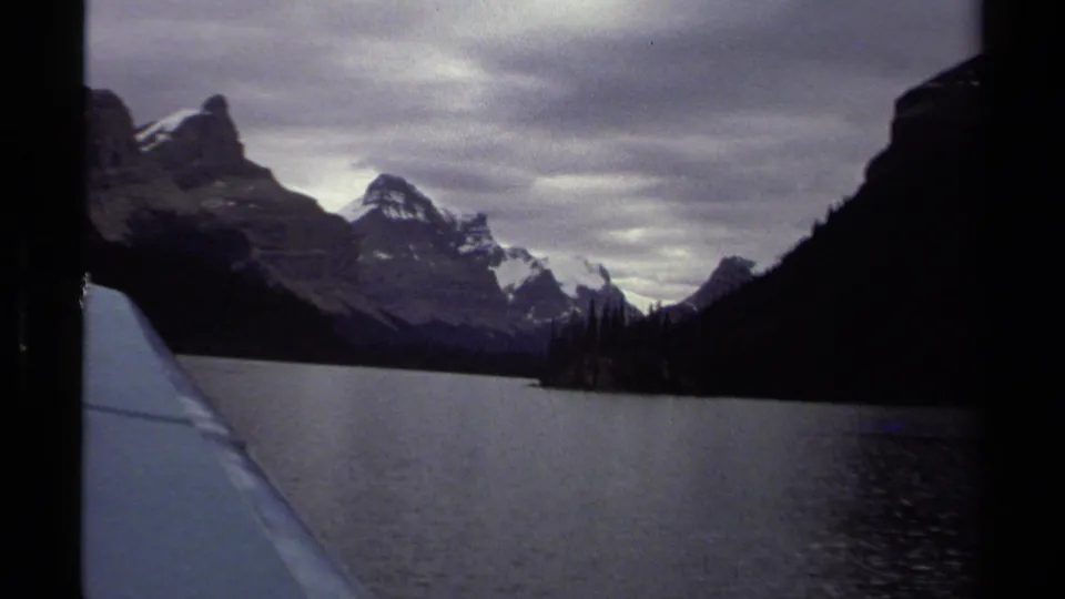 1979 British Columbia lake footage shows mountains and dark evergreen shoreline from a moving boat on overcast water.