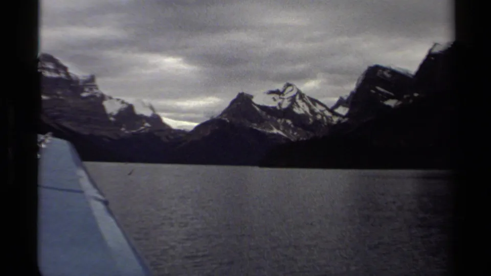 1979 British Columbia home-movie view from a moving boat across a calm lake toward snow-dusted mountain peaks.