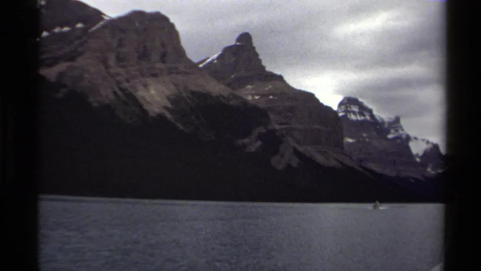 1979 8mm view of a rocky British Columbia mountain rising above lake water, with a small distant boat near the lower frame.