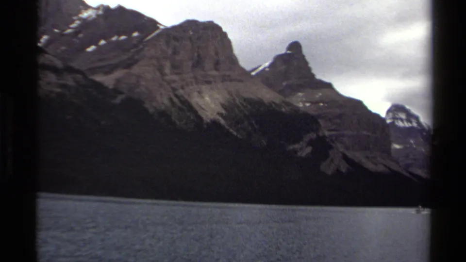 British Columbia mountain-lake scenery on 1979 8mm film, showing rugged slopes, snow traces, and a small distant boat.