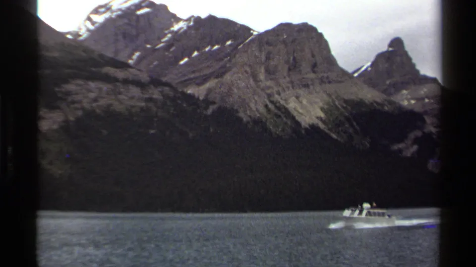 1979 British Columbia 8mm frame showing a small white motorboat near the lower edge of a mountain-lake vista.
