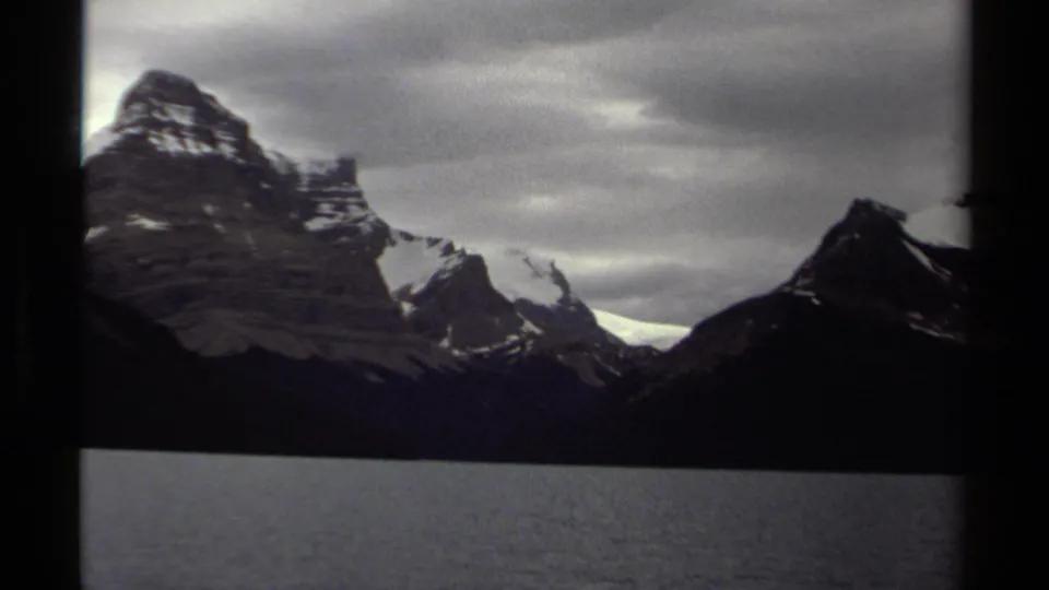 Vintage 1979 British Columbia 8mm frame showing rugged peaks, dark lake water, and an overcast mountain sky.