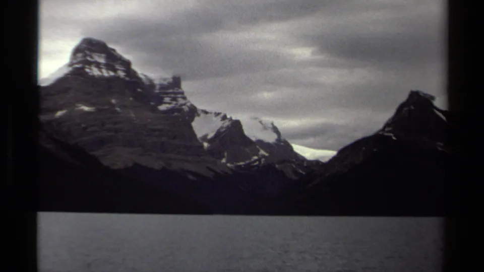 1979 8mm British Columbia travel frame with snow-marked peaks, a broad dark lake, and cloudy sky within visible film borders.