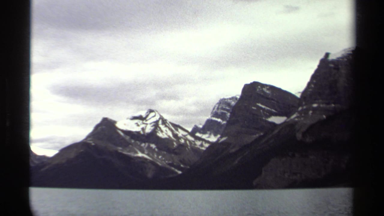 1979 British Columbia 8mm frame showing snow-capped mountain peaks across still water beneath an overcast sky.
