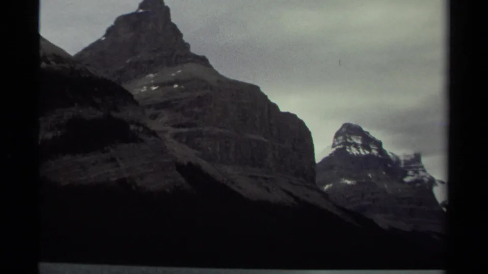 British Columbia mountain view with a prominent dark rocky peak and distant snow-capped summits in a 1979 8mm frame.
