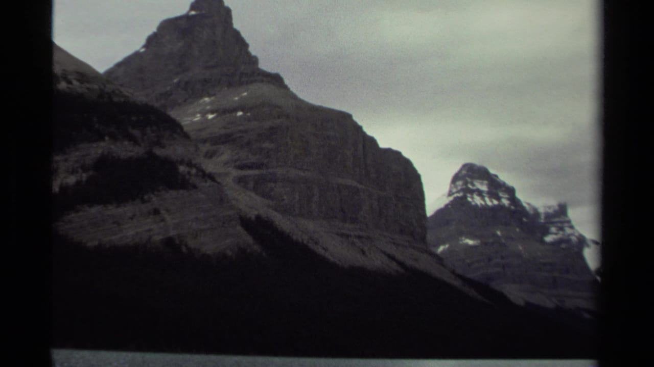 1979 8mm home-movie view of rugged British Columbia mountain peaks beneath a cloudy sky, with dark film edges visible.