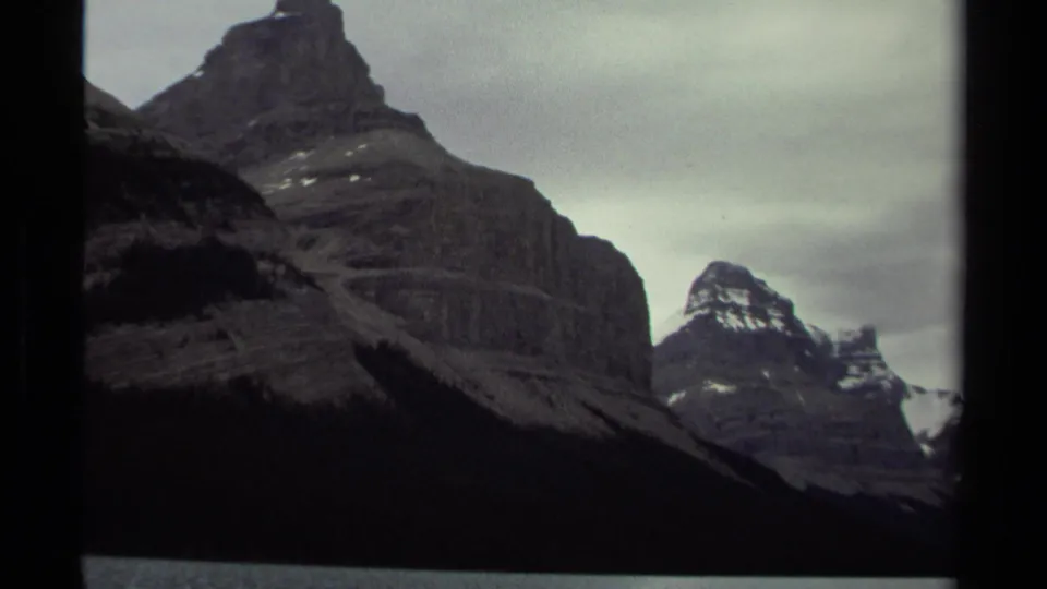 British Columbia mountain peaks appear in a dark 8mm frame, with snow traces and heavy cloud cover visible.