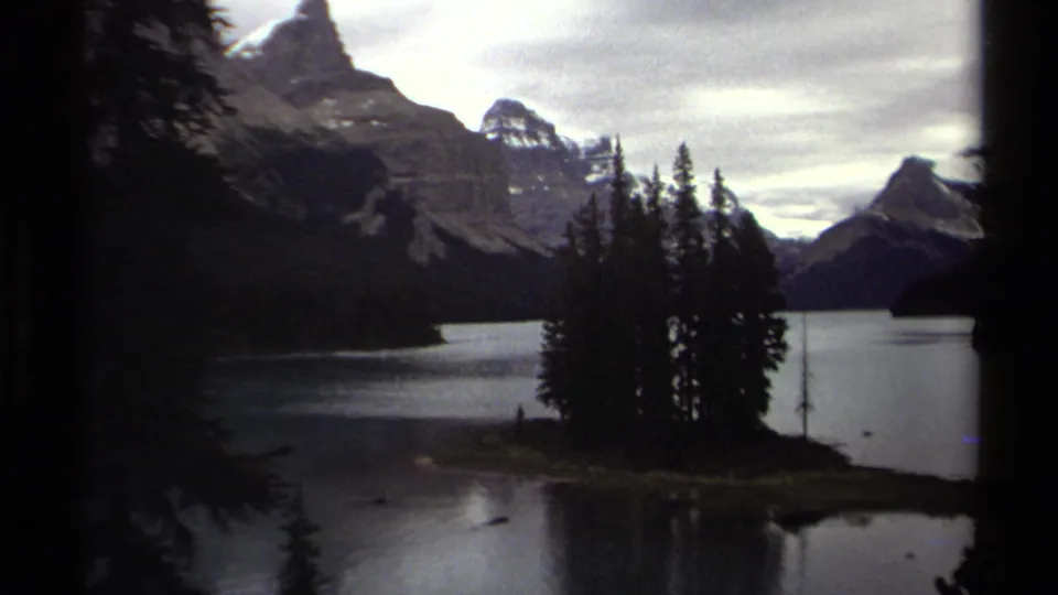 Vintage 8mm view of a British Columbia mountain lake, with a small wooded island silhouetted against distant peaks.