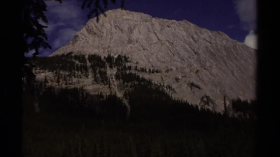 8mm frame of a broad rocky mountain face above evergreen forest, consistent with the British Columbia location metadata.