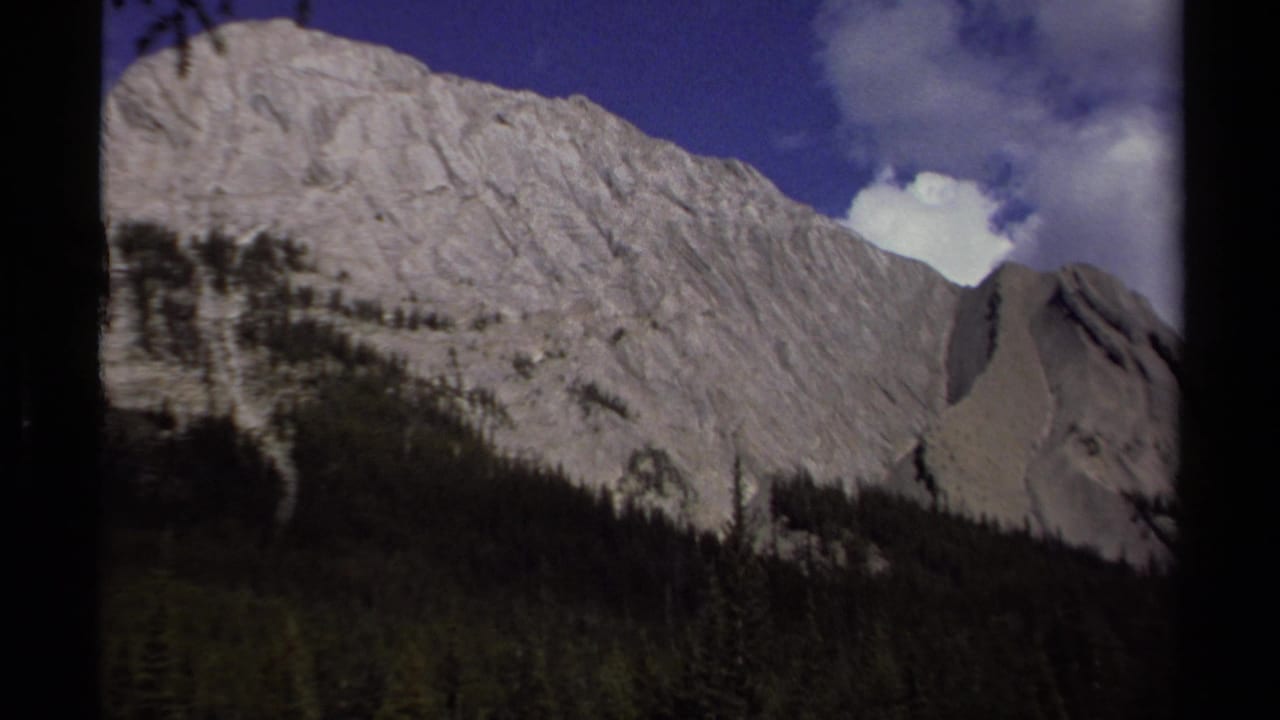 Mountain slope and forest line framed by clouds and dark film borders.