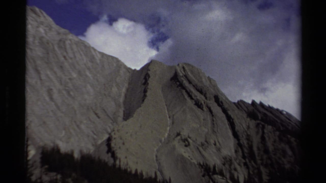 A British Columbia mountain ridge recorded on 8mm film in 1979, with steep stone slopes and cloud-filled sky.