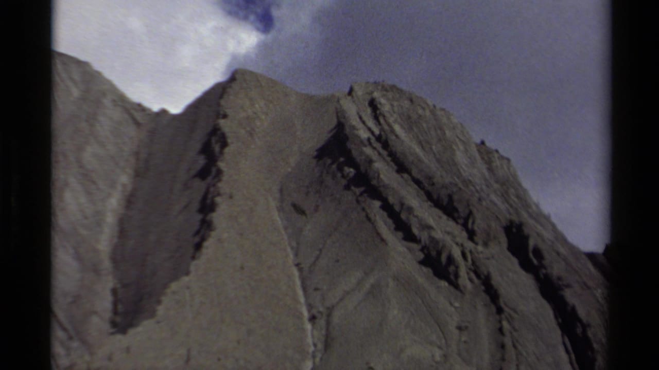 1979 British Columbia 8mm frame showing a steep layered mountain face under a pale sky, with visible gate edges.
