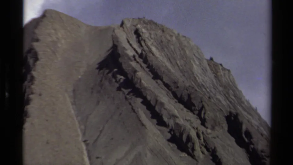 1979 British Columbia home-movie frame with a close view of a gray, stratified mountain peak and ridgeline.