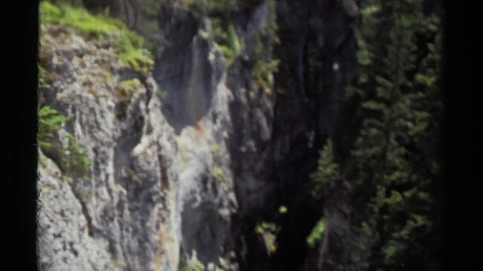 1979 8mm British Columbia canyon view showing gray cliff rock, mossy greenery, and deep shadowed forest gaps.