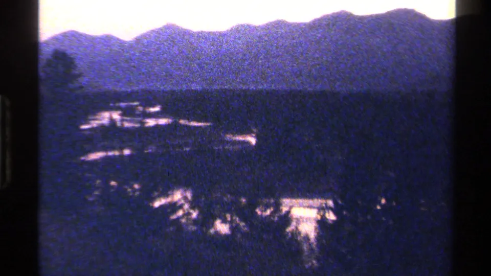 A grainy 1979 British Columbia landscape view shows water through a forested valley with mountains in the distance.