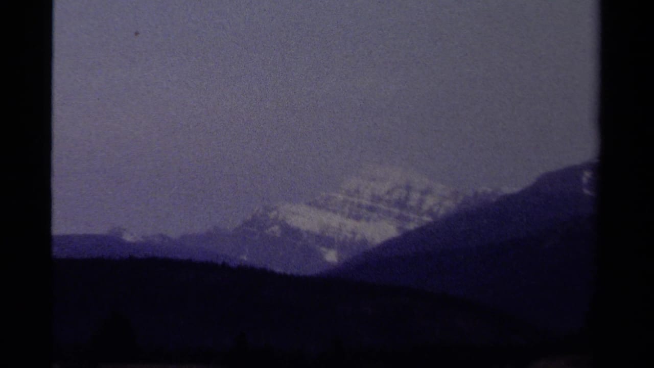 Snow-capped mountain peak beyond dark ridges under a muted sky.