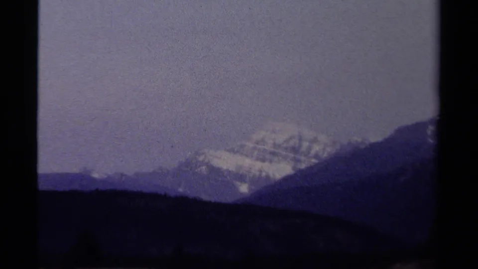 1979 British Columbia 8mm frame showing a distant snow-covered mountain range above dark foreground hills and a pale hazy sky.
