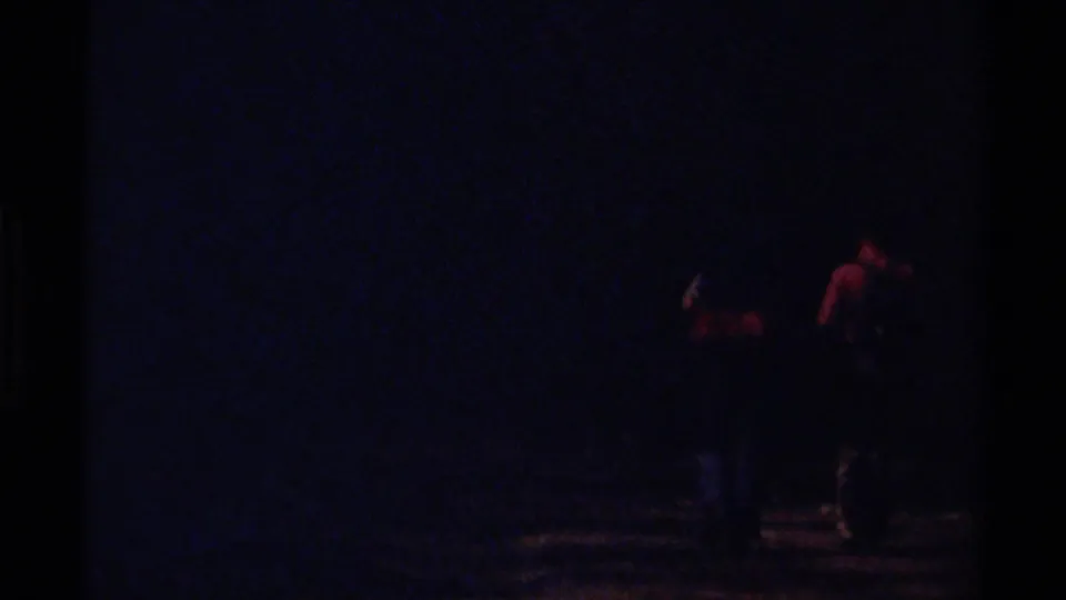 Underexposed 8mm frame from the British Columbia hiking clip, with faint figures on a forest road.