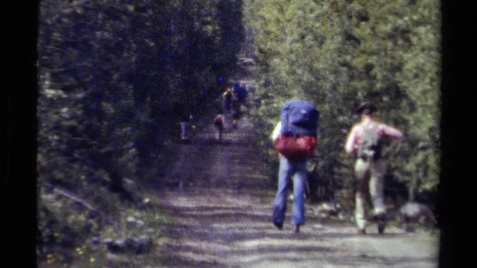A 1979 British Columbia home-movie frame shows backpackers walking away along a wooded dirt path.