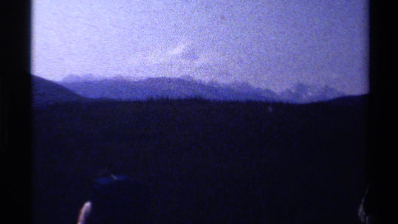 Distant mountain ridges and dark forest foreground with a partial figure at the bottom.