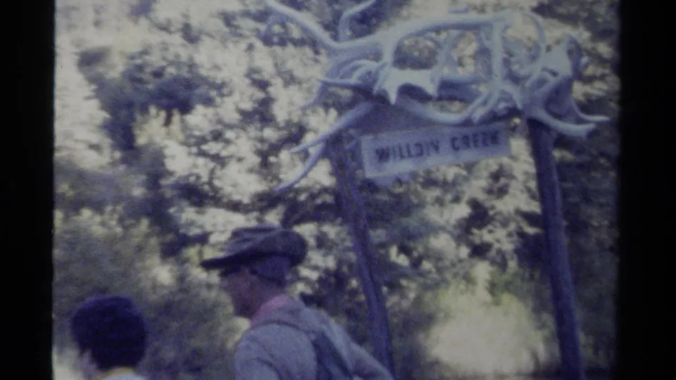 Visitors walk near the Willow Creek sign, with trees and creek-side vegetation visible in 1979 British Columbia footage.