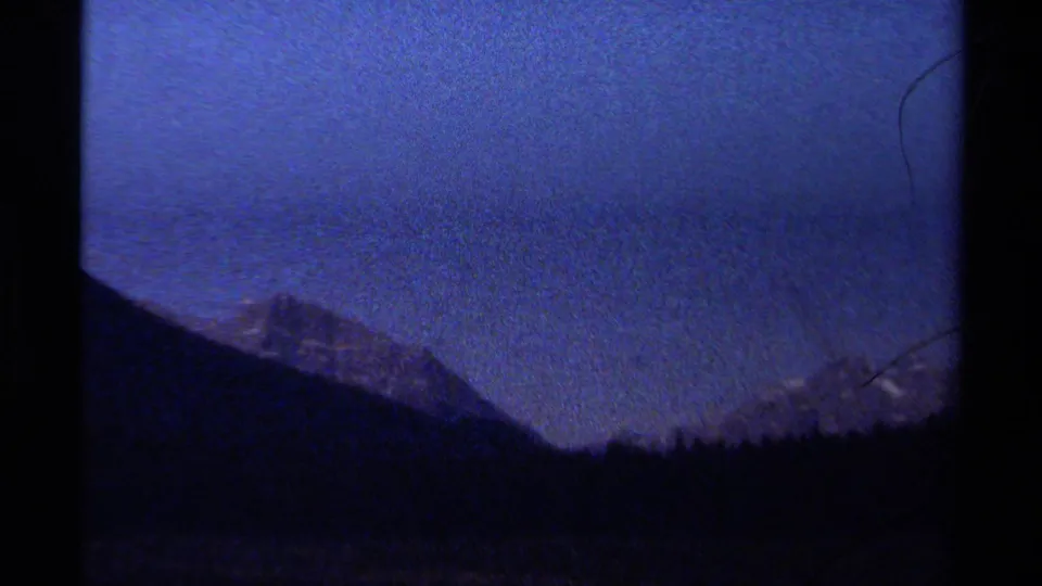 1979 British Columbia 8mm frame showing silhouetted mountains and forest ridge under a deep blue night sky.