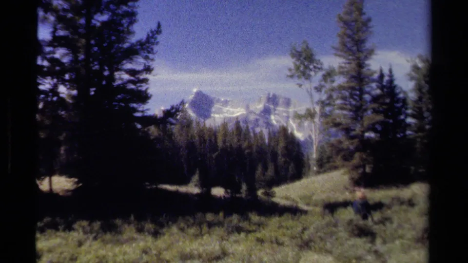 A wide mountain landscape shows meadow grass, conifer trees, and snow-streaked peaks in 1979 British Columbia footage.