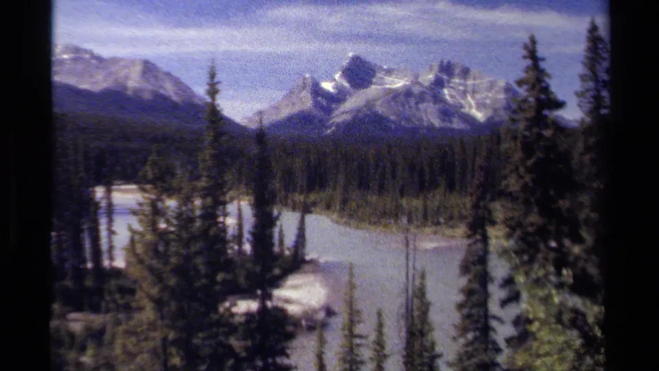 1979 British Columbia view of rugged snowy peaks above conifer forest and light-toned water, framed by dark film edges.