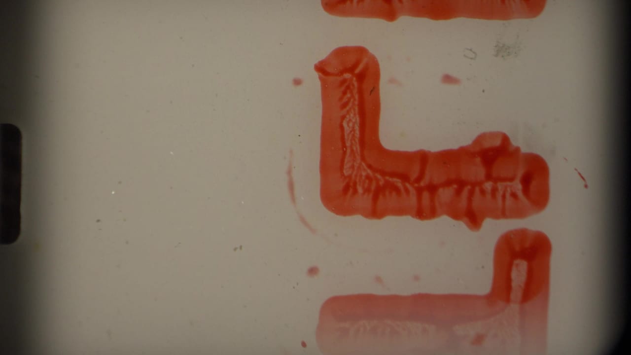 Film frame with pale leader area, red hand-drawn or processed markings, and dark gate borders.