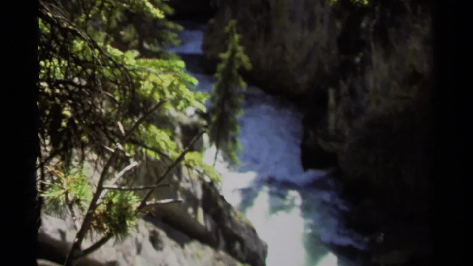 1979 8mm view of fast water moving through a British Columbia gorge, with trees and dark rock walls around the channel.