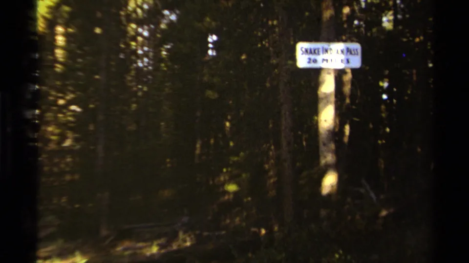 Soft 8mm frame of the Snake Indian Pass 20 Miles sign standing in a shaded British Columbia forest trail setting.