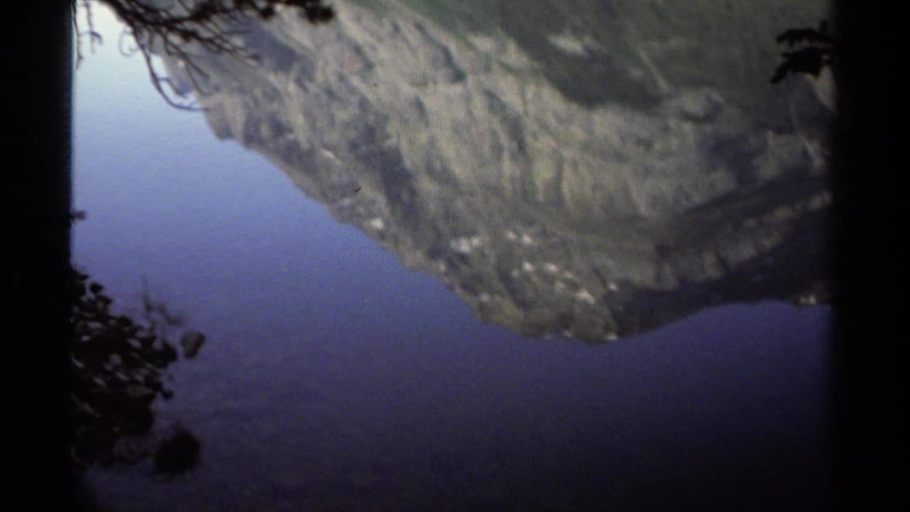 Mountain reflection on a quiet lake with dark tree silhouettes at the edges.