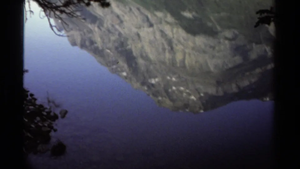 Muted 8mm view of a British Columbia mountain lake, with reflected rocky slopes and silhouetted trees.