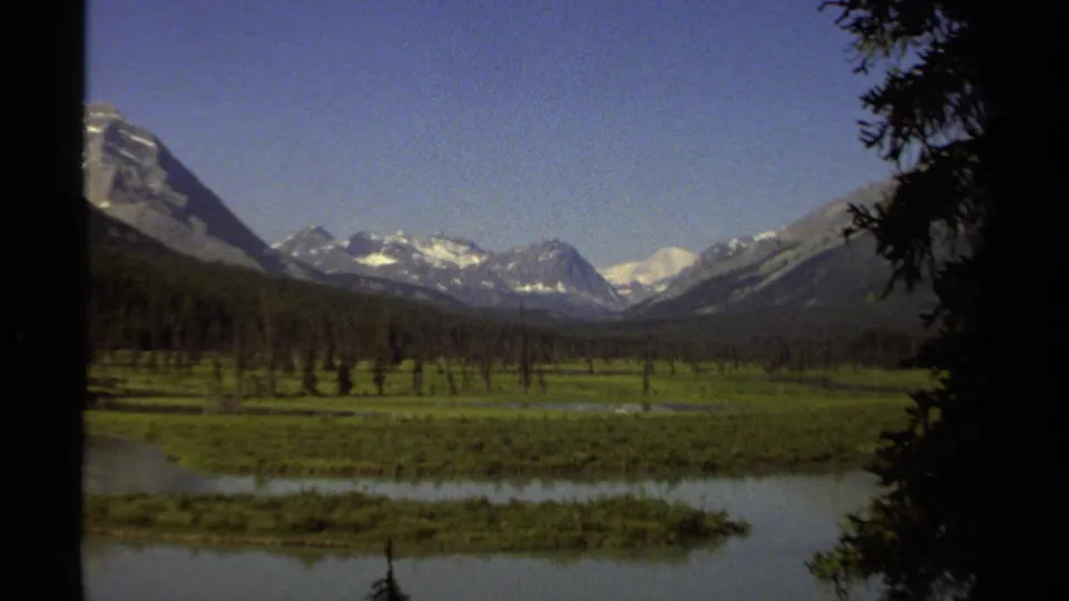 End frame of the 1979 British Columbia 8mm clip, with a calm lake, open green valley, forest, and snow-capped mountains in clear light.
