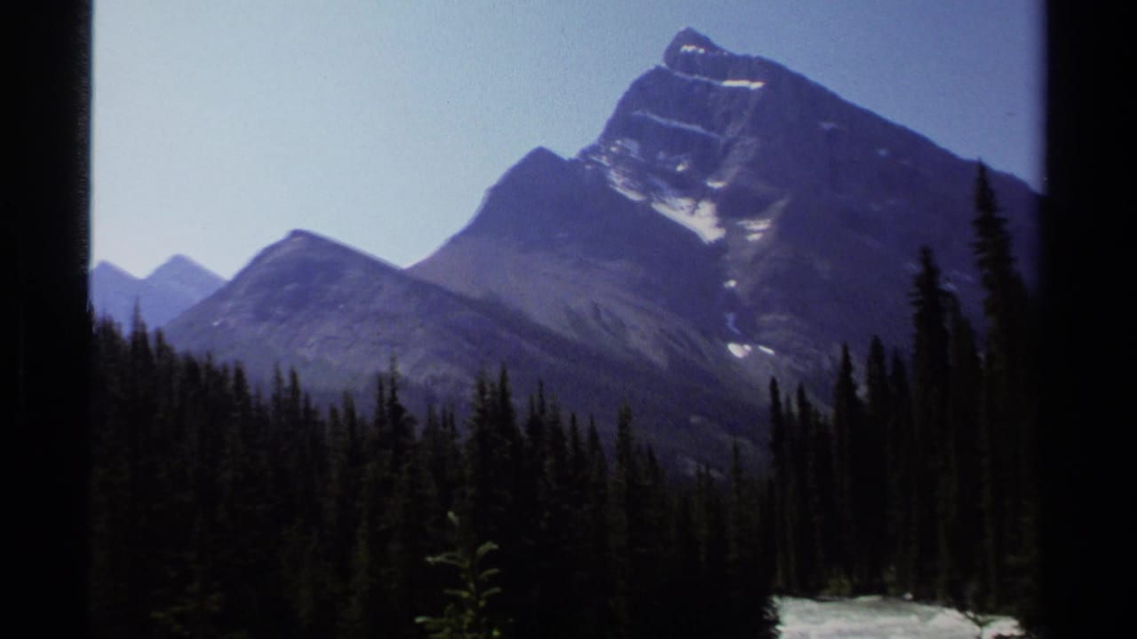 Mountain peak above pine forest with a strip of bright rushing water near the bottom edge.