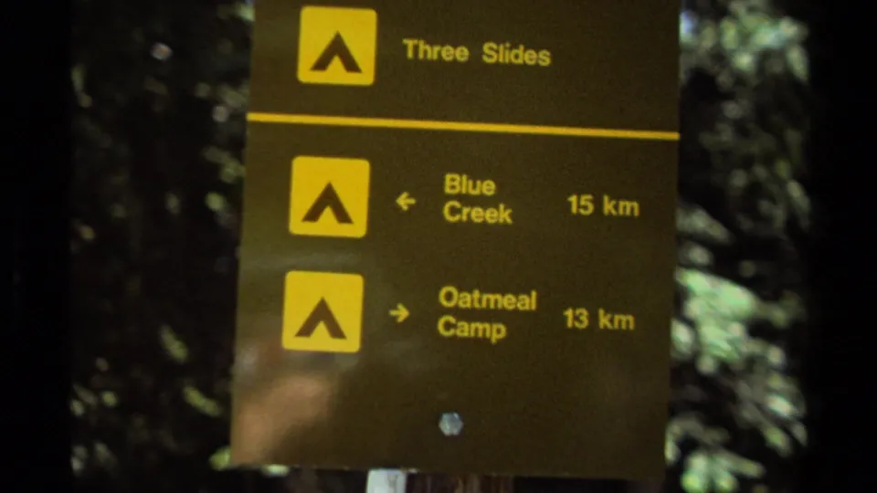 British Columbia trail sign on 1979 8mm footage showing Three Slides, Blue Creek 15 km, and Oatmeal Camp 13 km.