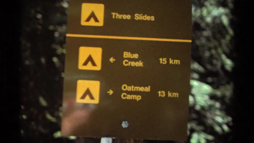 1979 British Columbia 8mm frame showing a brown forest trail marker with arrows and kilometer distances for nearby camping routes.