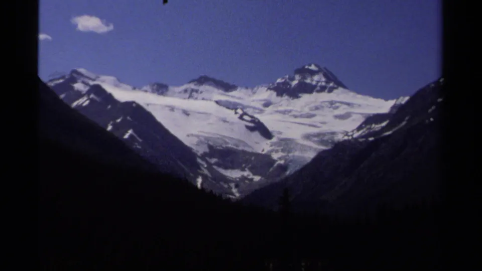 Closer 1979 8mm view of a British Columbia glacier between dark mountain slopes under clear sky.