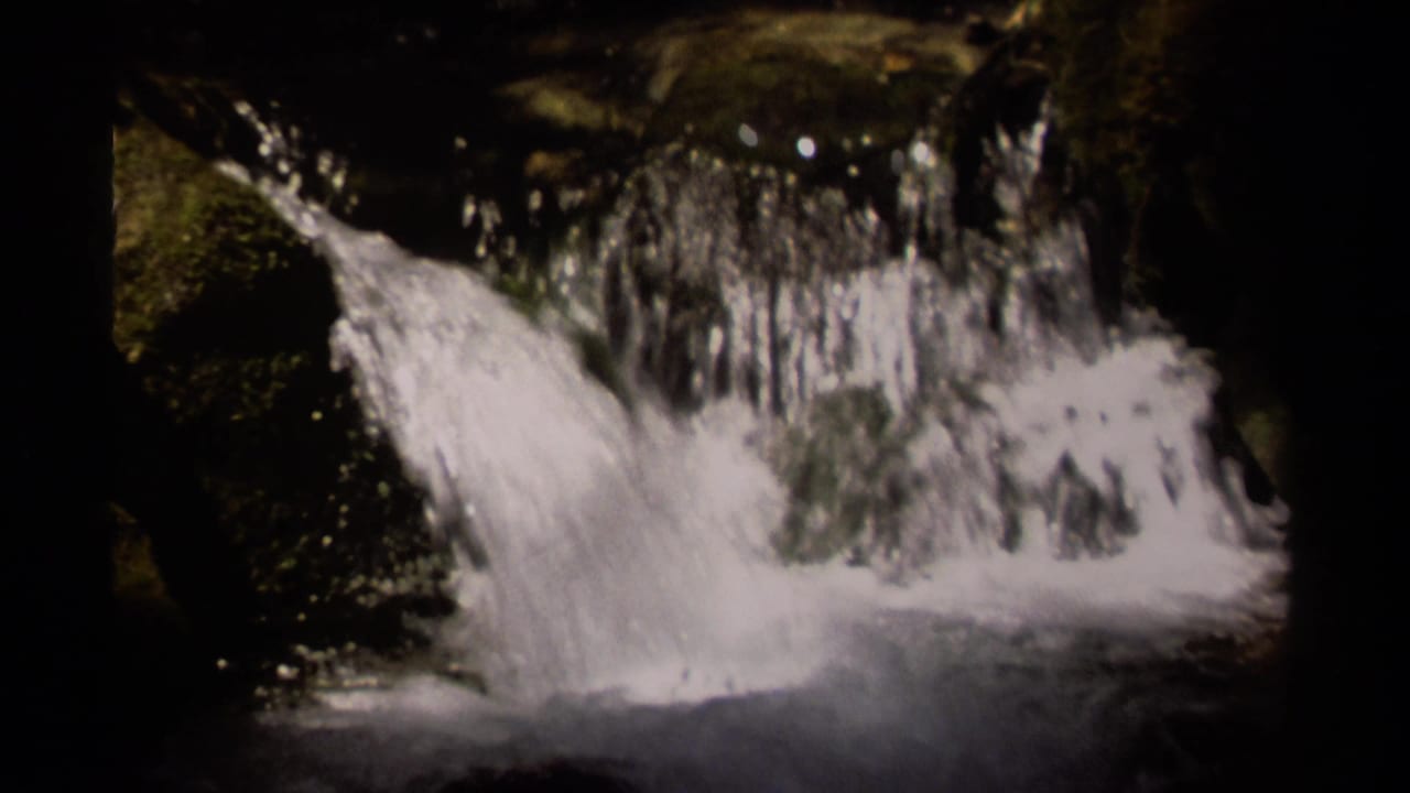 1979 British Columbia 8mm frame showing a small waterfall spilling over dark rock into shadowed water.