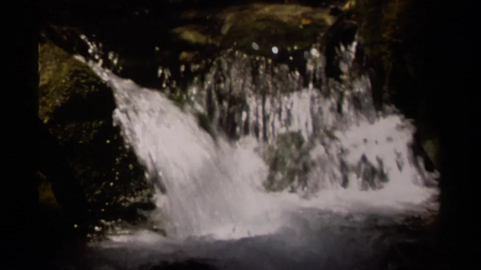 1979 British Columbia 8mm frame showing a small waterfall spilling over dark rock into shadowed water.