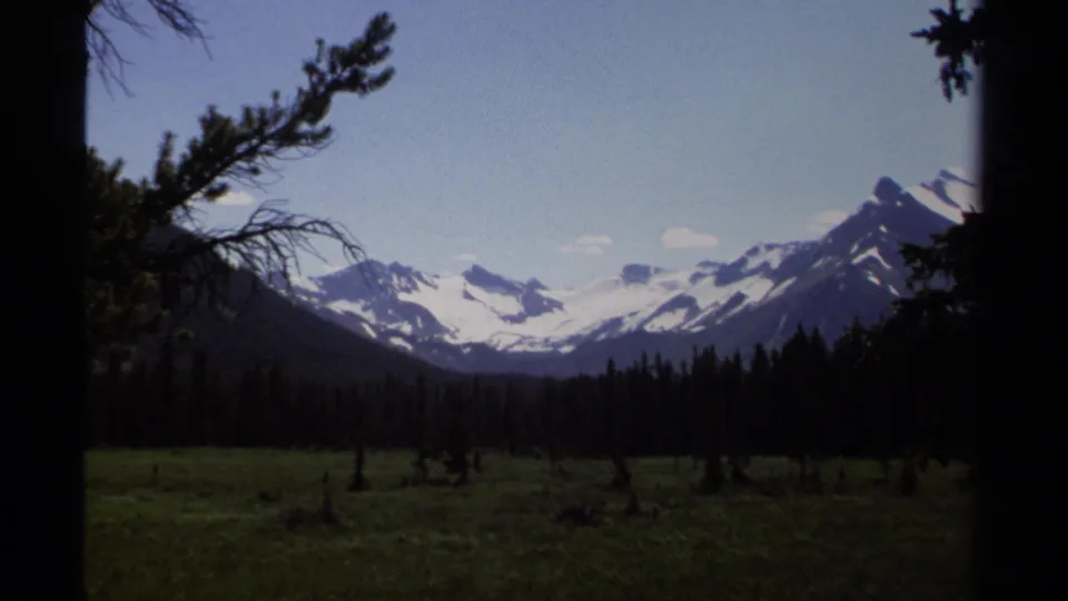 1979 British Columbia mountain vista framed by dark conifers, with snow-capped peaks in the distance.