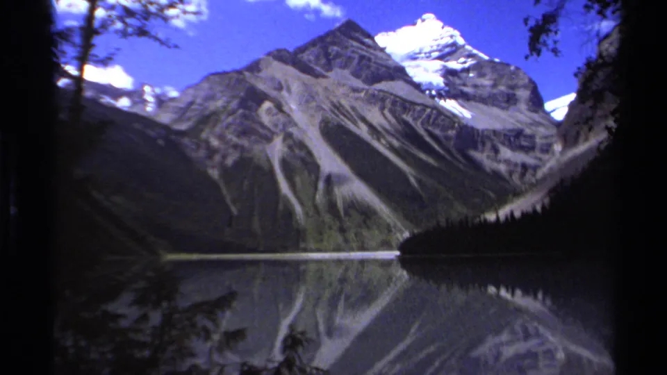 The lake view holds on rugged British Columbia peaks, bright clouds, and mirrored water, with dark forested slopes framing the 1979 home-movie scene.