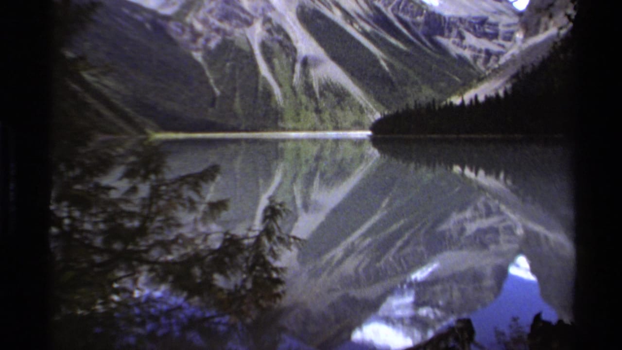 Alpine lake reflecting steep mountains, with trees and shoreline in shadow.