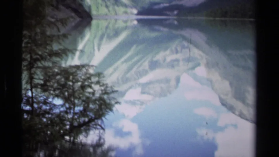 Upside-down 8mm view of a British Columbia mountain lake, with conifer shoreline, pale clouds, blue sky, and mirrored peaks.