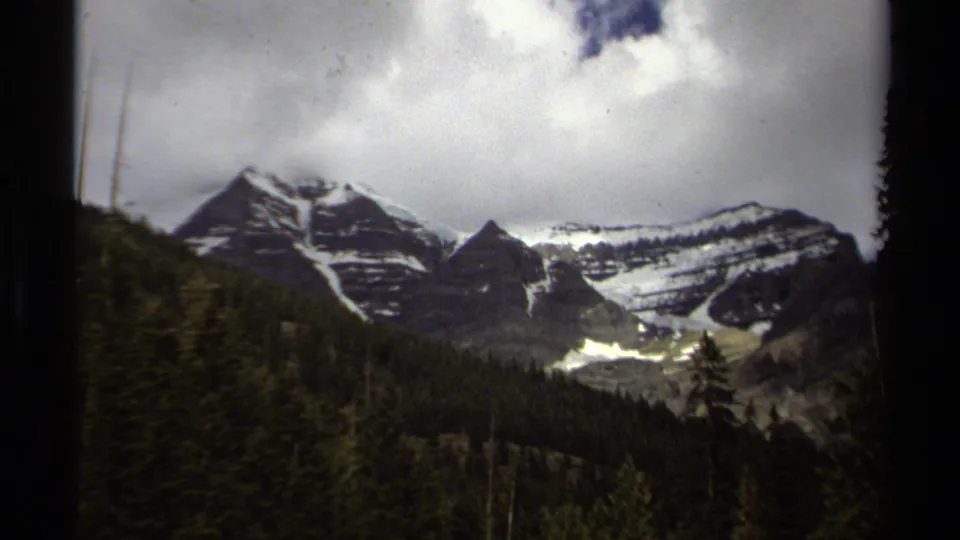 1979 8mm view of British Columbia mountains under cloud, with snow bands and dense forest in the valley.