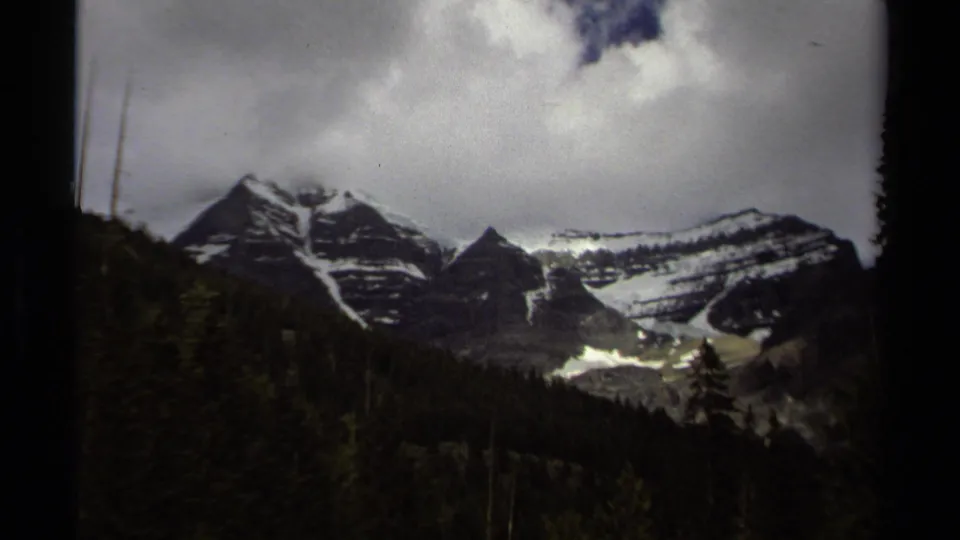 1979 British Columbia landscape showing a snow-streaked mountain range, dark forested valley, and heavy cloud cover.