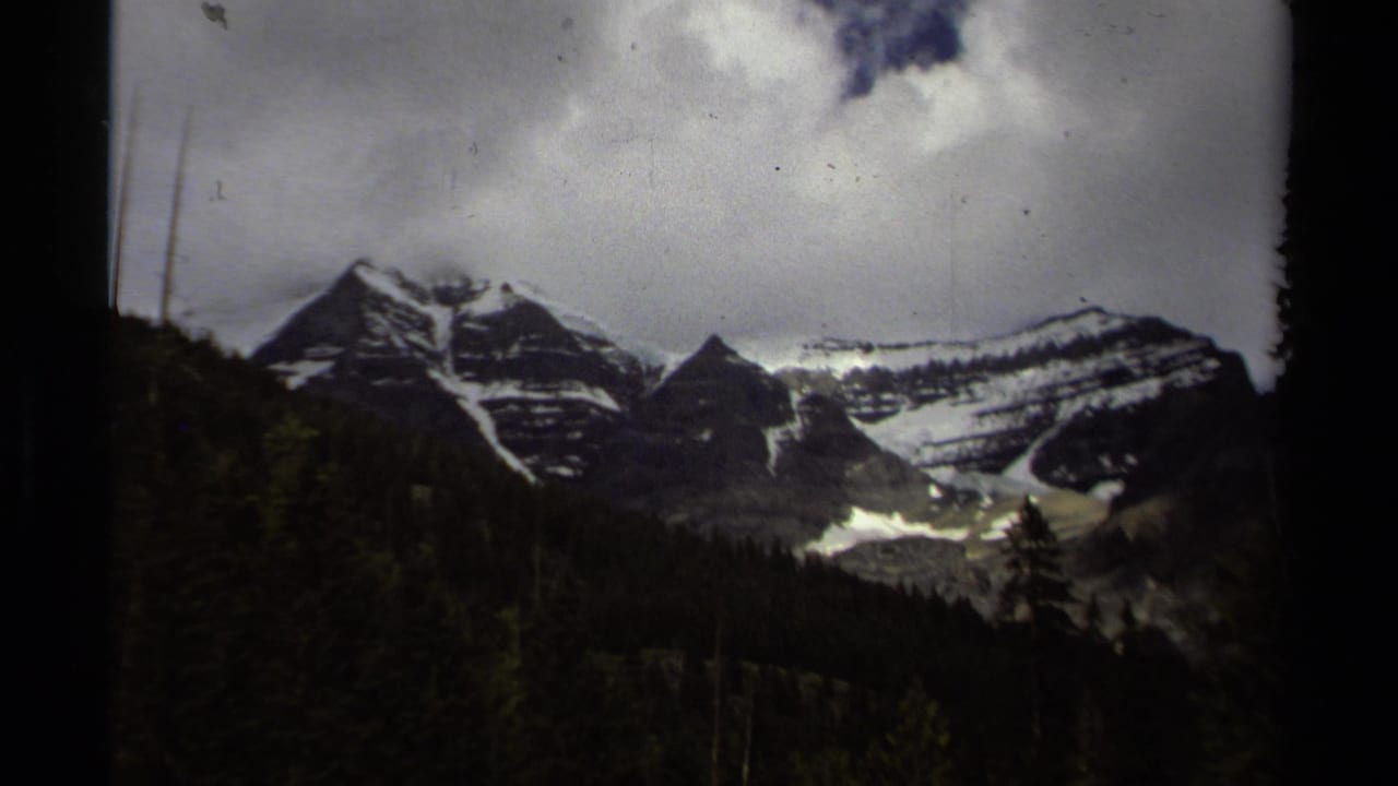 1979 British Columbia 8mm view of snow-streaked mountains rising above evergreen forest beneath a cloudy sky.