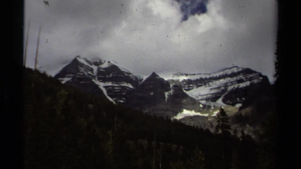 1979 British Columbia 8mm view of snow-streaked mountains rising above evergreen forest beneath a cloudy sky.