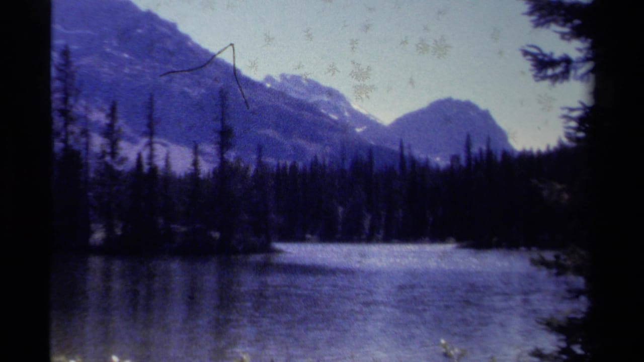 Mountain lake scene with forested shoreline and peaks beyond the water.